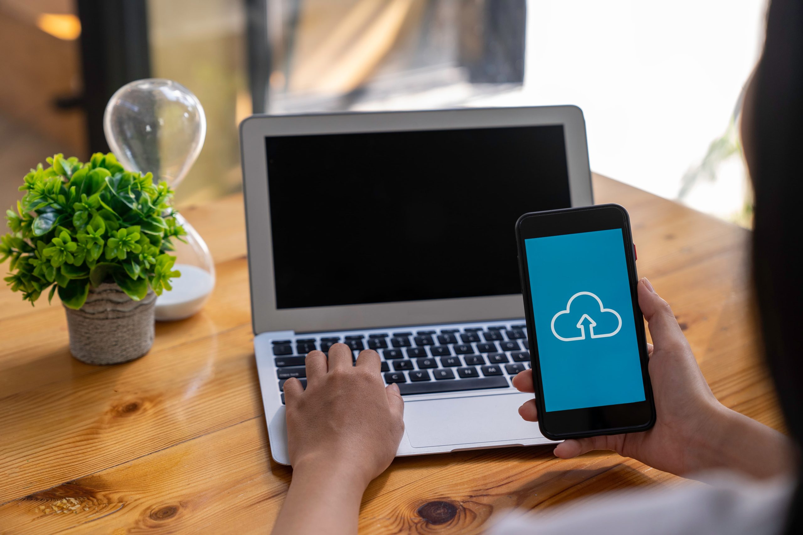 Persoon gebruikt laptop en smartphone met cloud backup icoon op het scherm voor veilige gegevensopslag