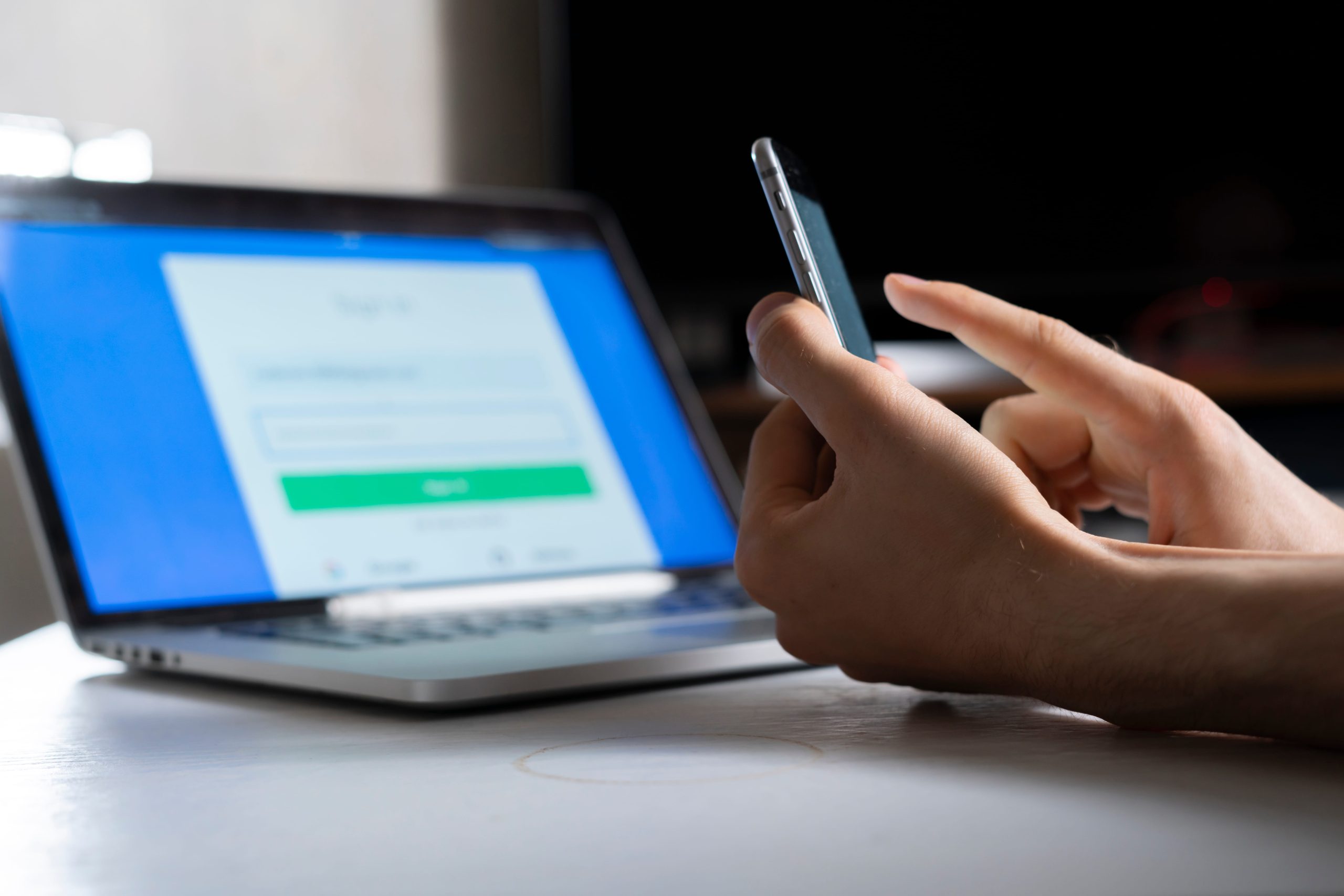 Persoon gebruikt smartphone voor Microsoft 365 MFA authenticatie met laptop op de achtergrond