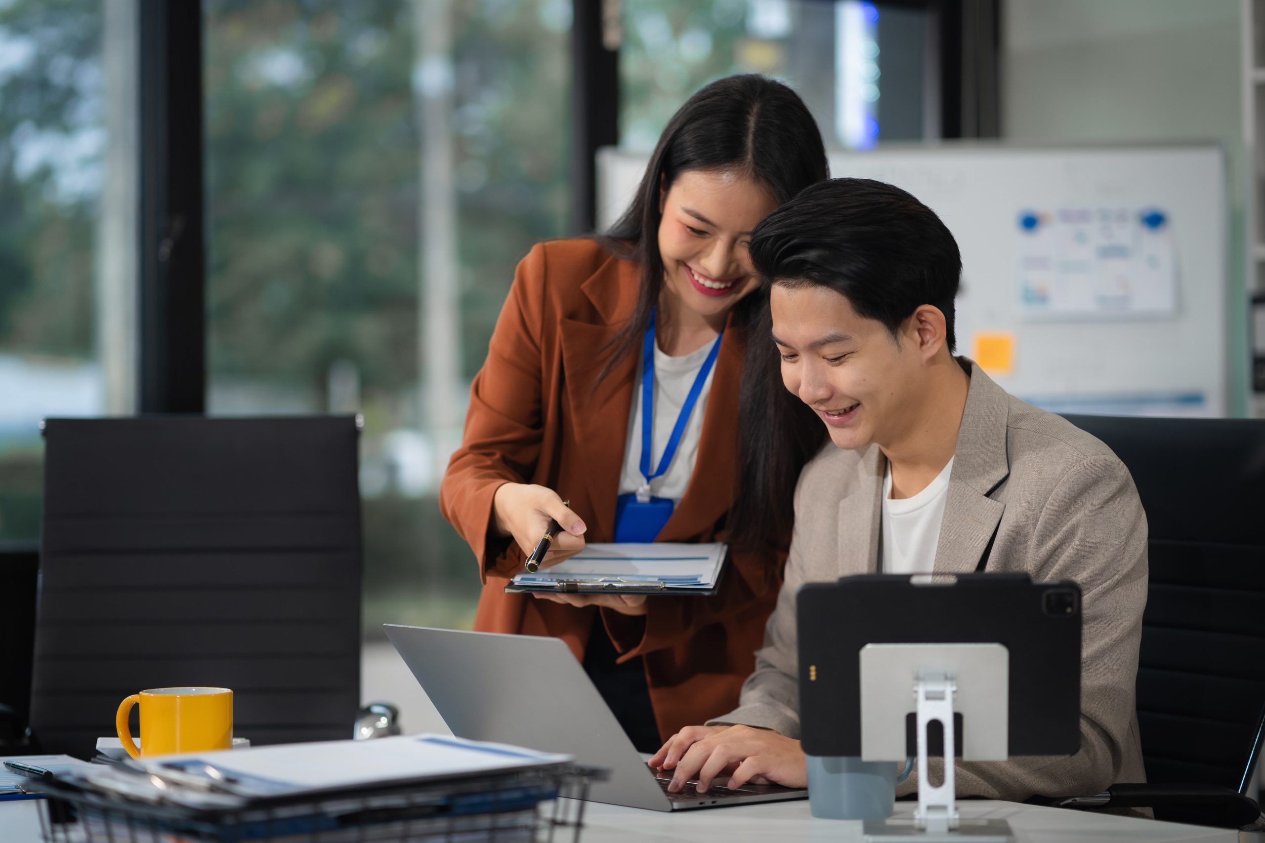 Twee collega’s bespreken gegevens op een laptop, gebruikmakend van OneDrive Backup in een moderne kantooromgeving